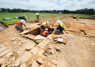 Five construction workers in the foreground and three in the background inspecting the ground for archaeological artefacts during the excavation at Sydney Metro's White Hart Inn site.
