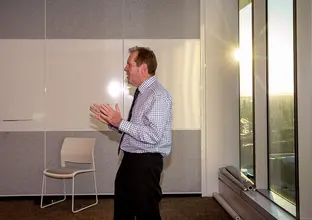 A man presenting in a boardroom while the sun sets in the background over the city skyline.