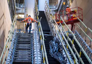 One construction worker stands at the top installing escalators at Central Station while another is in a lift next to him.