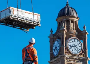 Low angle shot of construction worker viewing solar panels being lifted by a crane with the Central Station clock tower in the background