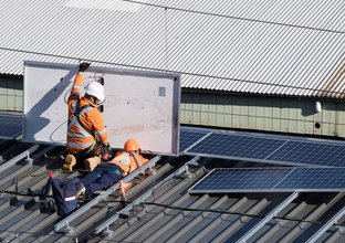 Two construction workers installing solar panels on Central Station's rooftop