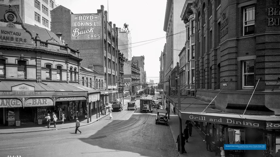 Black and white photo of people walking down Elizabeth Street looking south from the corner of Hunter Street
