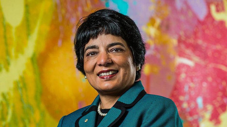 Dr Marlene Kanga standing infront of a colorful background, smiling at the camera