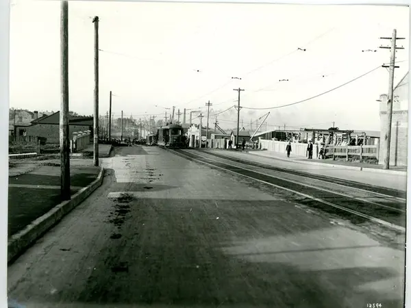 A black and white image of Cooks River Road, Sydnebgam from 1928 showing the road  with old tram tracks to the right of the image and a tram in the background (Image Courtesy of Inner West Council Library and History)