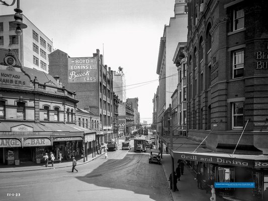 Black and white photo of people walking down Elizabeth Street looking south from the corner of Hunter Street