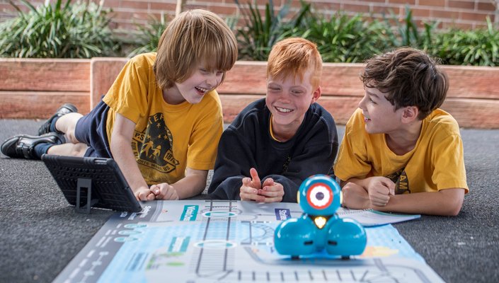 Three students from Petersham Public School smiling behind the dash robot that is sitting on top of an alignment map