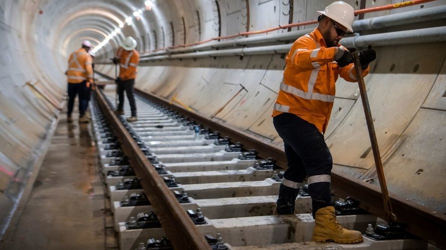 Three construction workers in high viz and hard hats are working on the installation of the track in the tunnel under Sydney Harbour.