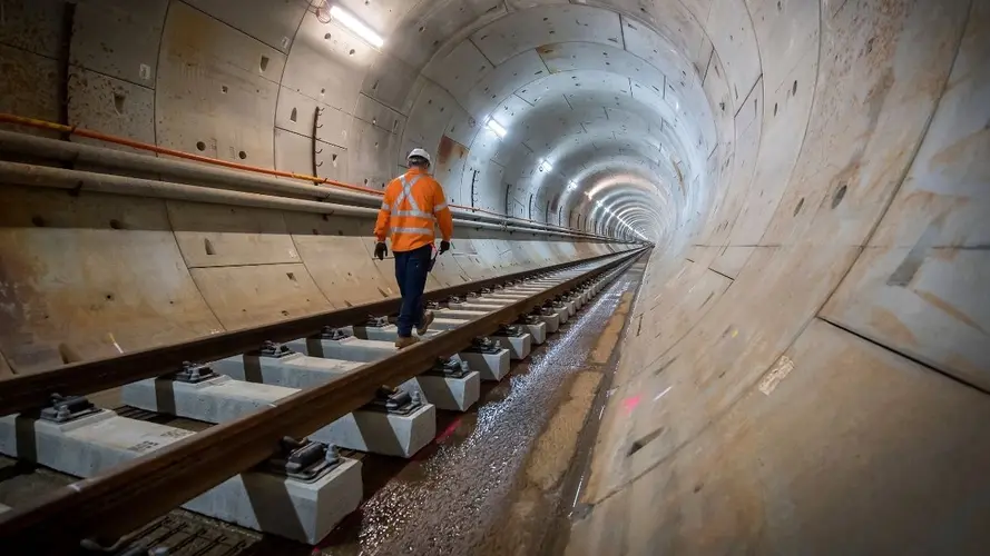 Construction worker with back to photo is walking along the track inside the tunnel