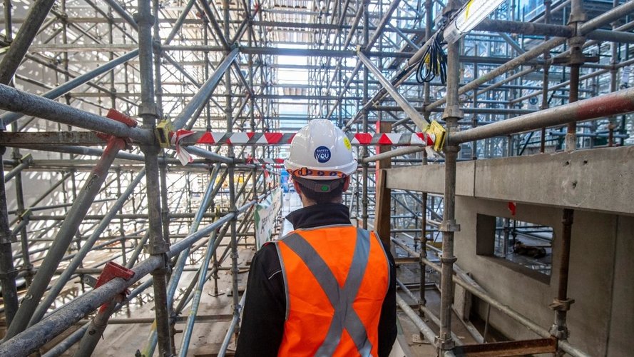 Construction worker with back to photo is standing amongst scaffolding