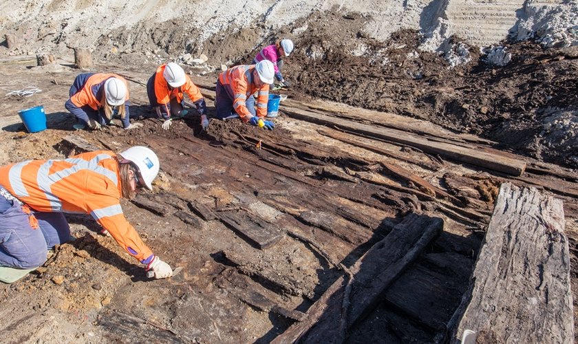 Archaeologists in high vis and hard hats are on their hands and knees while working in the excavation area at the future site of Barangaroo Metro Station where an old boat was found.