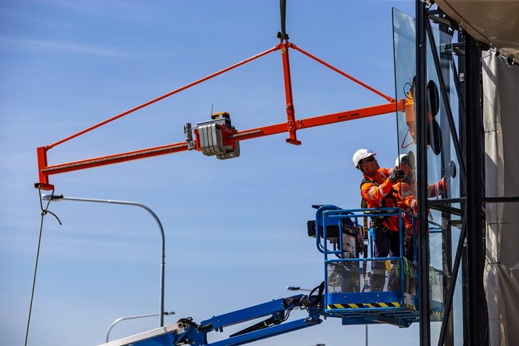 A close up shot of two construction workers installing glass windows from a cherry picker at Sydney Metro's Kellyville Station. 