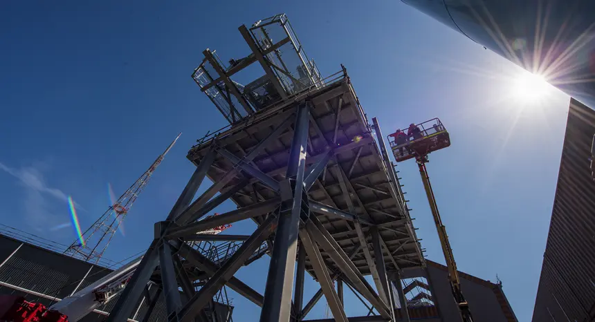 An on the ground view looking up under the conveyer belt as two construction workers are inspecting above from a cherry picker at Sydney Metro's Chatswood Drive.