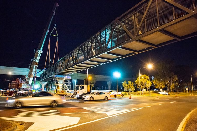 An on the ground view showing the final segment of the pedestrian walkway that has been crane lifted into place  at night at Sydney Metro's Kellyville Station.