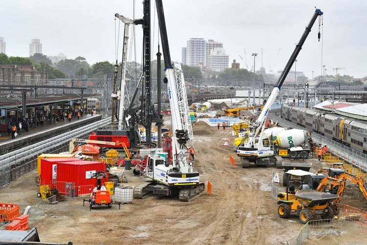 An arial view looking across at the construction site of the Sydney Metro station box at Central Station with many heavy machinery on the ground between the platforms. 
