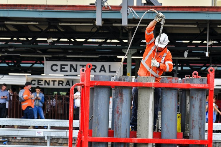 A close up shot of a construction worker spraying pipes in the station box at Sydney Metro's Central Station. 