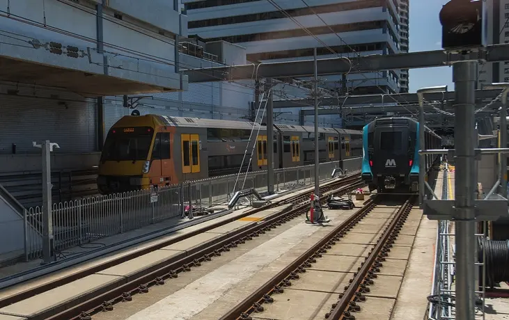 An on the ground view looking across the station platform as a Sydney Metro Train arrives at the platform next to a Sydney Trains train at Chatswood Station.