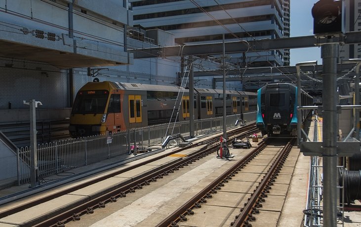 An on the ground view looking across the station platform as a Sydney Metro Train arrives at the platform next to a Sydney Trains train at Chatswood Station. 