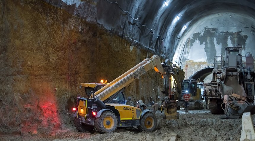 An on the ground view inside the cavern showing two excavators and a larger machine in the background as a construction worker is walking through the machines with a head torch on at Sydney Metro's Martin Place Station.
