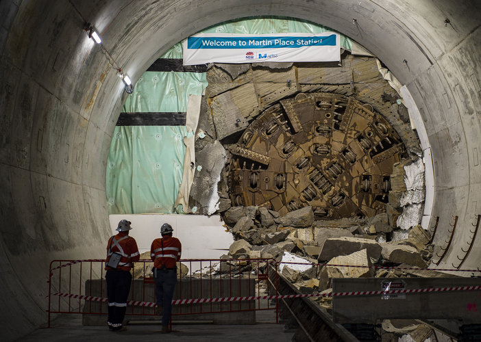 The cutterhead of tunnel boring machine Mum Shirl can be seen breaking through the wall at Martin Place Station. Two construction workers in high viz can be seen watching.