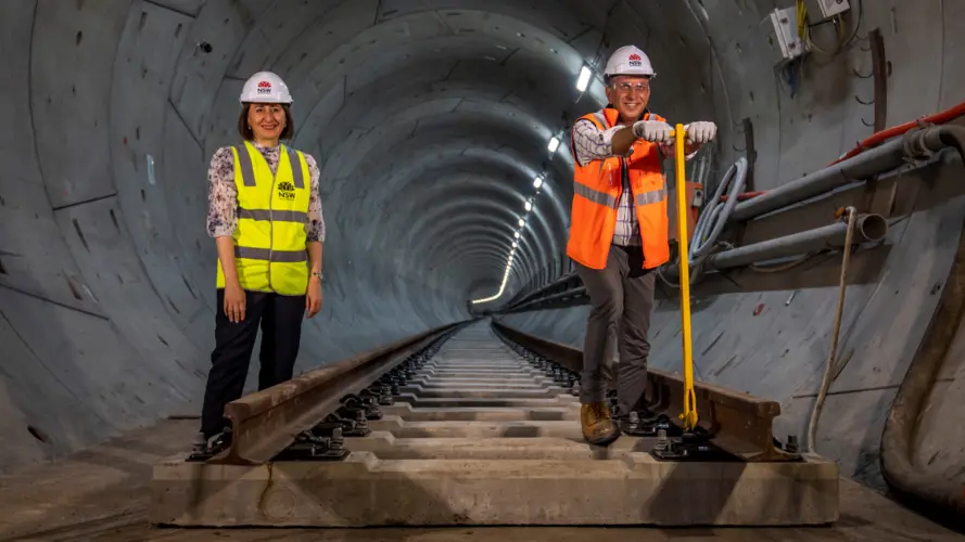 The NSW Premier and Minister for Transport standing on newly laid rail track in the tunnel at Chatswood.