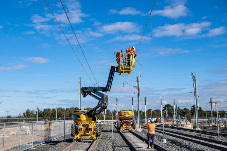 A wide angle view of construction workers on a cherry picker lift as the overhead works continue as part of the expansion of the Sydney Metro Trains Facility in Rouse Hill.