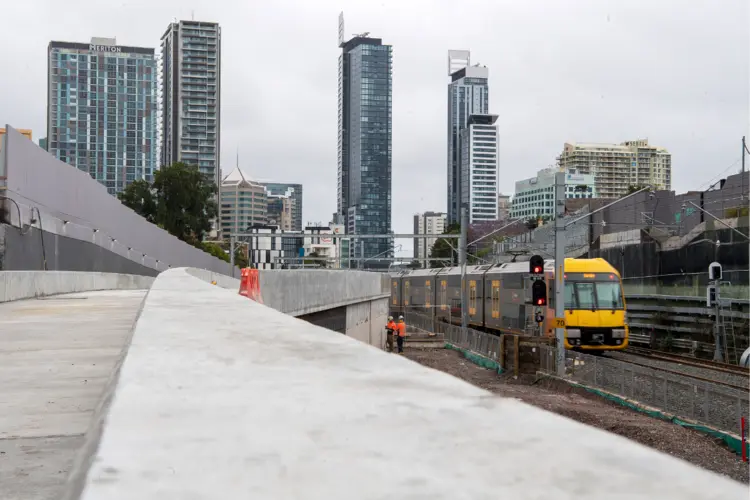 A Sydney train passing by the Chatswood Dive site. There are high rise buildings in the background.