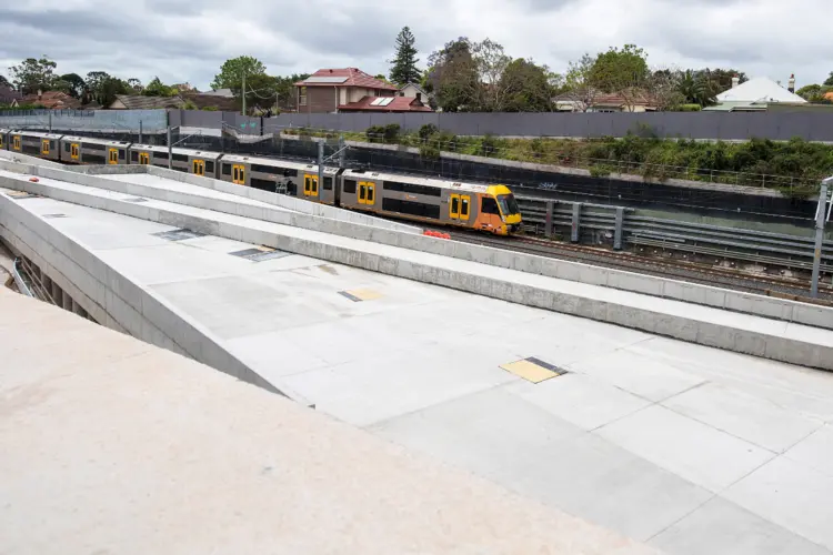 A Sydney train passing by the Chatswood Dive site. There are houses in the background.