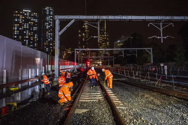Tracks are being reconnected by construction workers at night between Artarmon and Chatswood stations. Sydney city skyline can be seen in the background.
