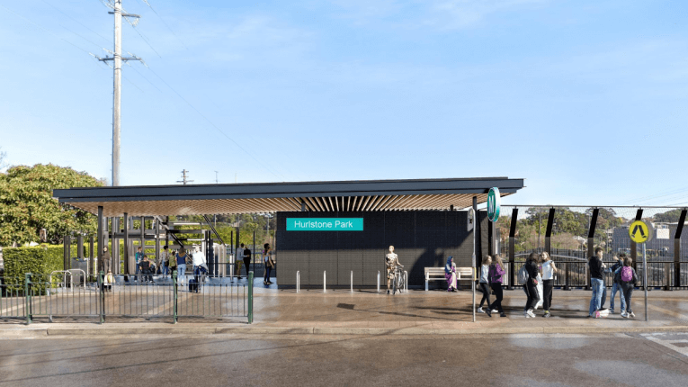 An artists impression of the entry to Hurlstone Park Station. There are people walking around and blue sky in the background.