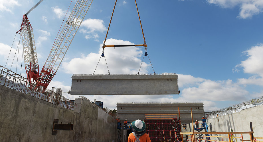 Large concrete beams are being installed by a crane in the station box of the Bella Vista Station construction site.