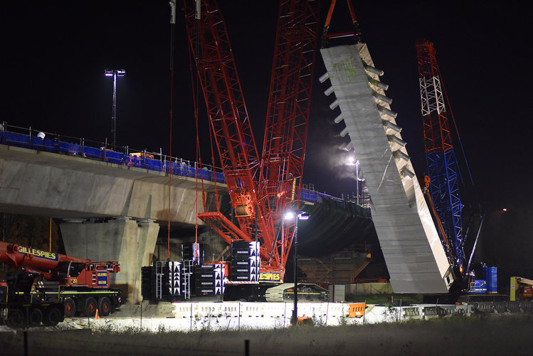 An on the ground view looking at the construction of the skytrain bridge tower as a crane lift is lifting a section of the bridge tower from the ground at night at Sydney Metro's Rouse Hill. 