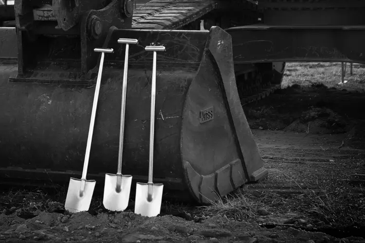 A black and white image of three shovels sitting against a heavy machinery vehicle as construction gets underway on the Sydney Metro West project.