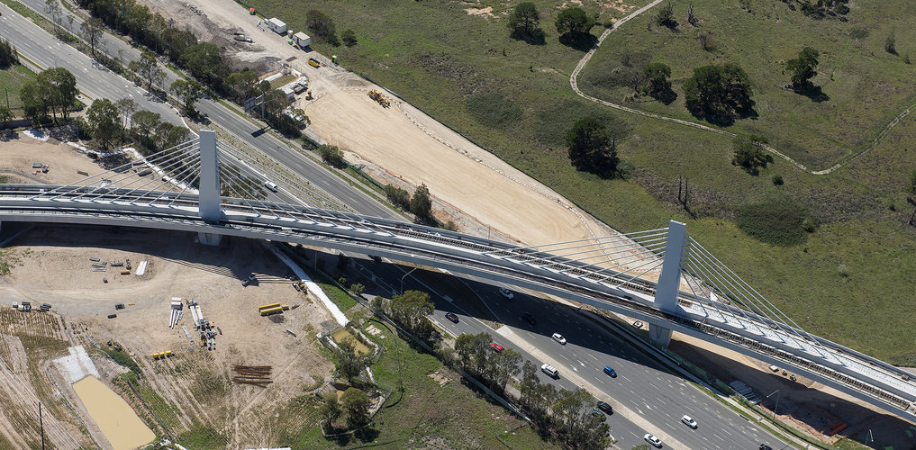 A bird's eye view of Sydney Metro's Windsor Road bridge being constructed, there are cars traveling on the road below.