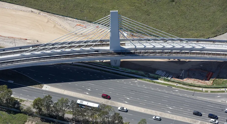 A bird's eye view of Sydney Metro's Windsor Road bridge being constructed, there are cars traveling on the road below.