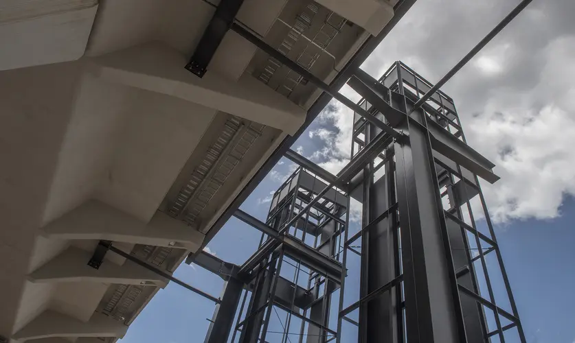 An on the ground view looking up at the construction of the two towered lift shaft sat Sydney Metro's Kellyville Station from underneath the platform concourse.
