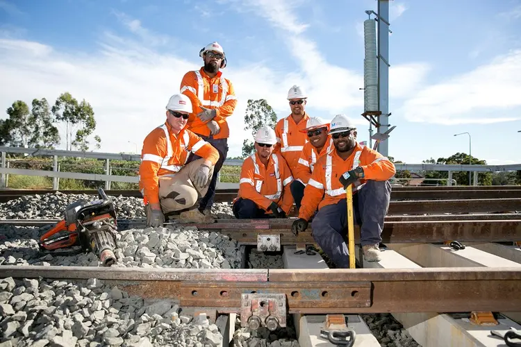 A group of six construction workers sitting on the train tracks as the final track is laid on the Sydney Metro Northwest line in April 2018.