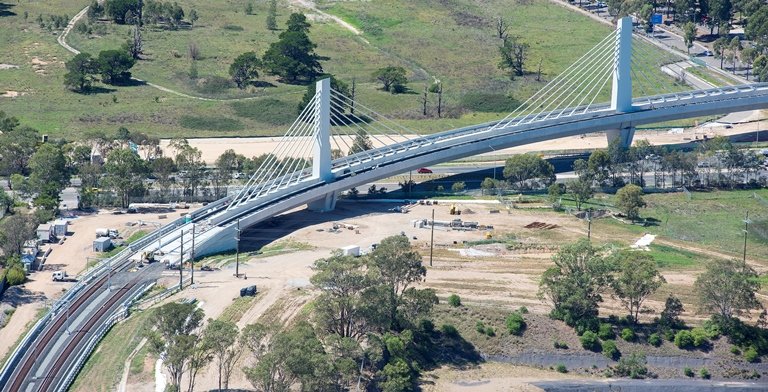 A bird's eye view of the completed bridge section showing cable stayed design with a train running along the tracks.
