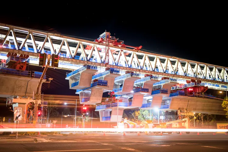 An on the ground view looking up at the construction of the final span of Sydney Metro's skytrain bridge at night.