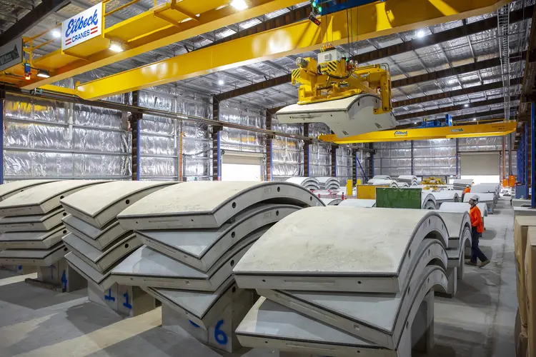 An on the ground shot showing rows on precast concrete segments lined up for production with a machine liftin one of the segments into place at Marrickville precast facility.