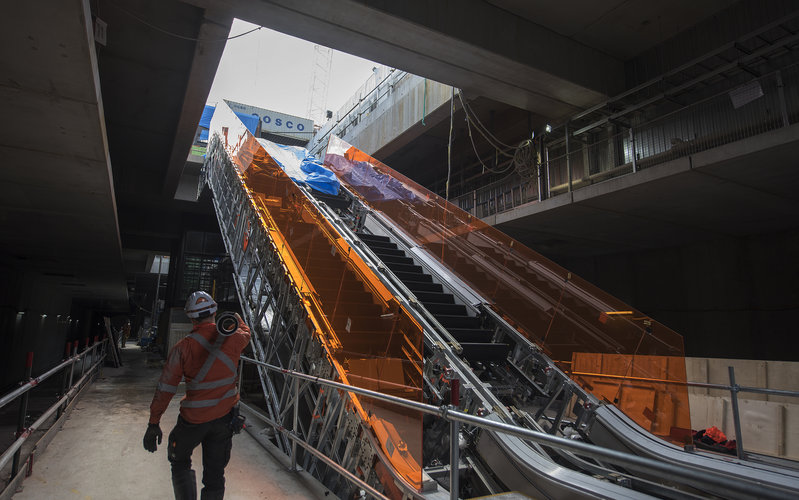 An on the ground view showing the construction of the escalators at Sydney Metro's Norwest Station as a construction worker walks past carrying material them. 