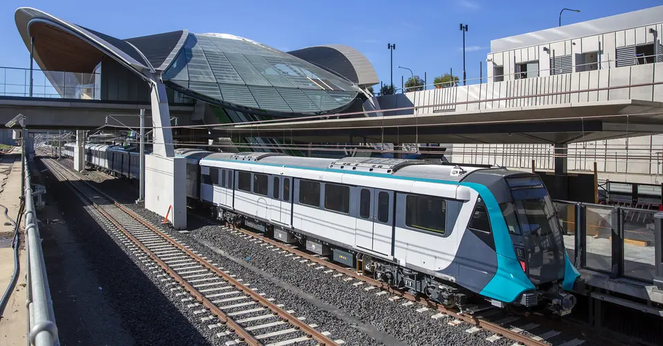 An above the ground view looking down at the first Sydney Metro train arriving at the platform of the city's first metro station showing the station in the background.