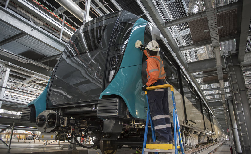 A close up shot showing a Sydney Metro employee in full PPE up standing on a foot ladder cleaning the new Sydney Metro train.