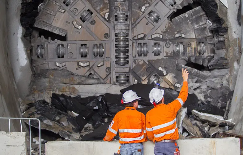 An on the ground view of two construction workers inspecting the tunnel breakthrough from Tunnel Boring Machine (TBM) 1 Elizabeth at Sydney Metro's Hills Showground Station.