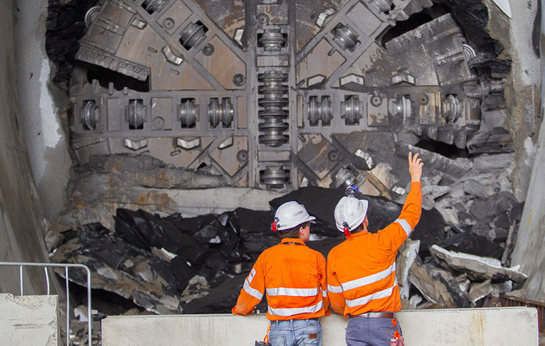 An on the ground view of two construction workers inspecting the tunnel breakthrough from Tunnel Boring Machine (TBM) 1 Elizabeth at Sydney Metro's Hills Showground Station. 