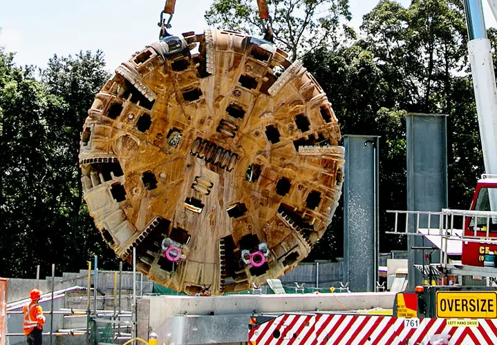 An on the ground view showing a construction worker inspecting the cutterhead of Tunnel Boring Machine (TBM) being retrieved at Sydney Mero's Epping station.