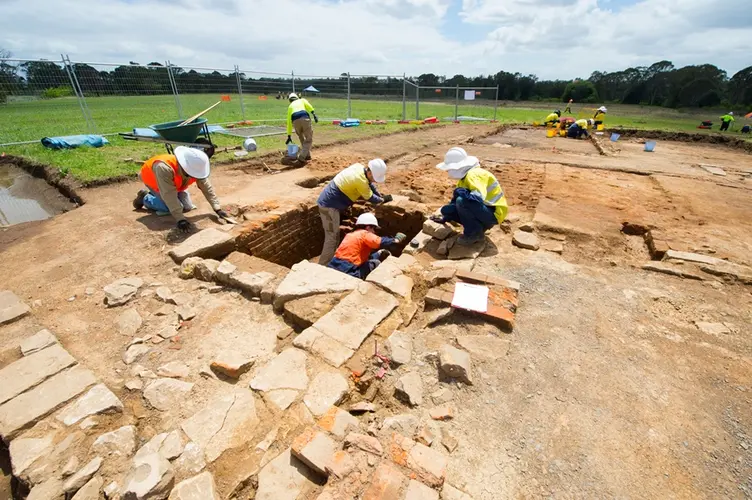 Five construction workers in the foreground and three in the background inspecting the ground for archaeological artefacts during the excavation at Sydney Metro's White Hart Inn site.