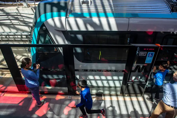 An Arial view of a Sydney Metro train stopped at the platform with commuters standing outside the screen doors.
