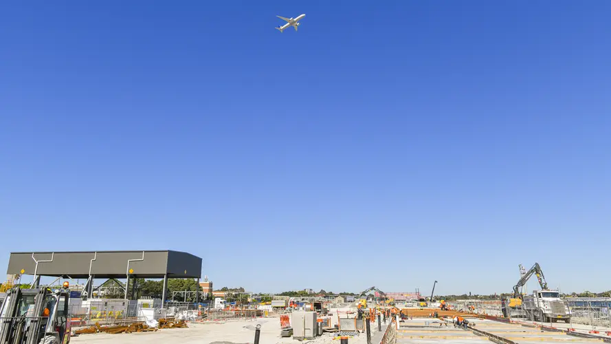 A wide angle of Sydney Metro Trains Facility South Yard under construction in Marrickville with a airplane flying above it.