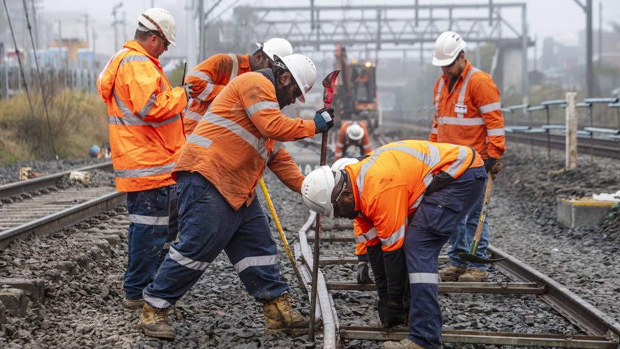 A group of construction workers in orange high-vis are placing the new metro tracks into place at Bankstown Station.