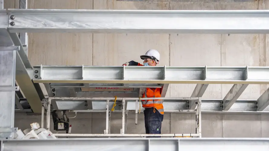 A construction worker is standing between steel beams while installing them at Waterloo Station.